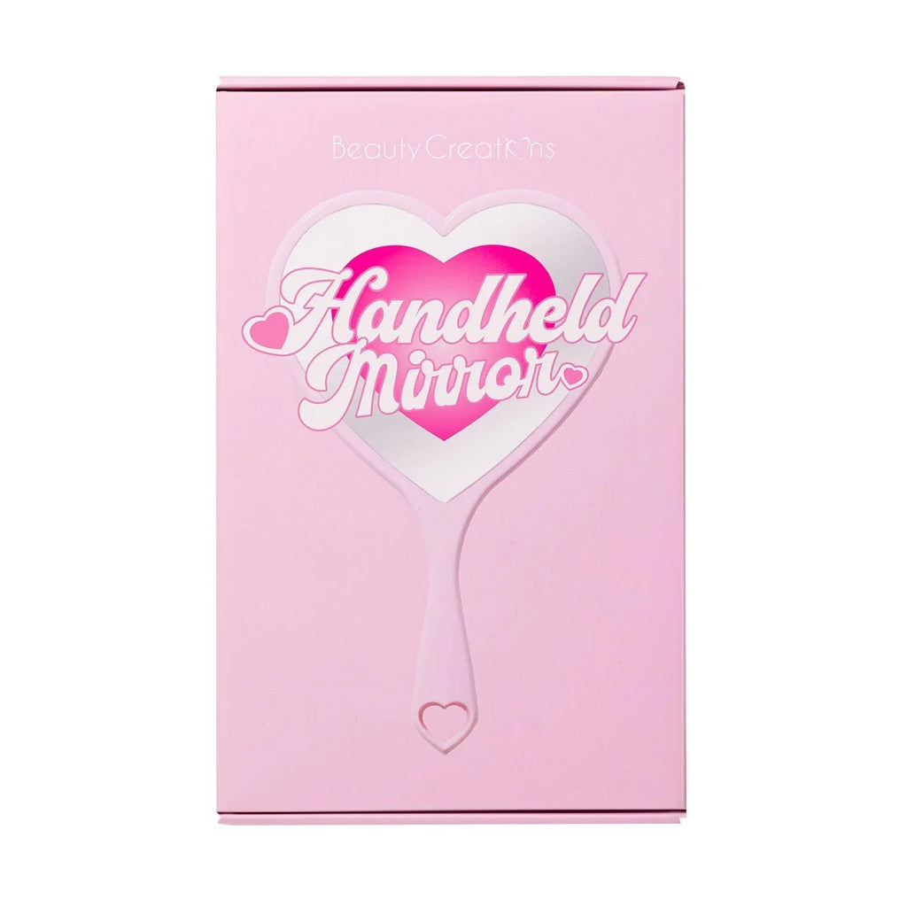 Caja de empaque rosa con un gran gráfico de espejo en forma de corazón y las palabras "Handheld Mirror" en caligrafía blanca sobre un corazón rosa, con el nombre de la marca "Beauty Creations" impreso en la parte superior.