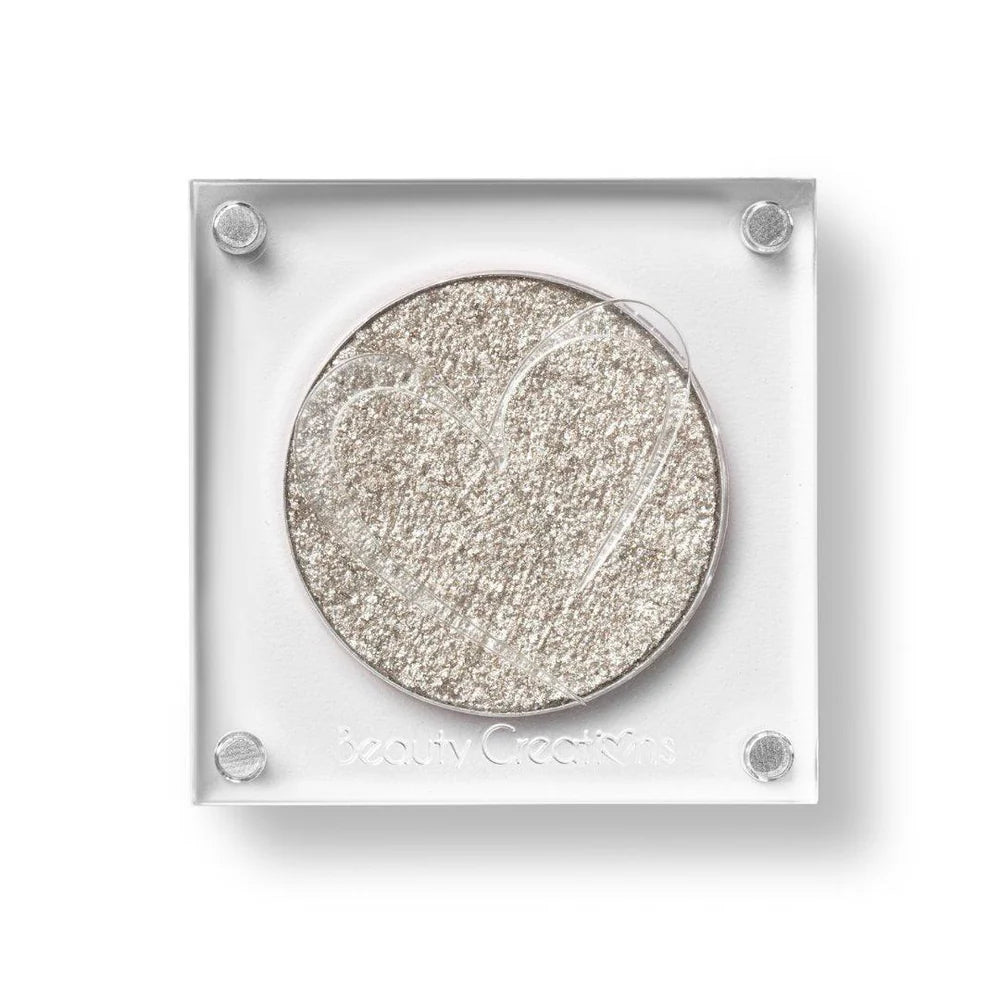 Un estuche cuadrado de sombra de ojos de Beauty Creations en acrílico transparente con un hueco redondo de sombra plateado claro brillante, con un recorte en forma de corazón en la tapa.