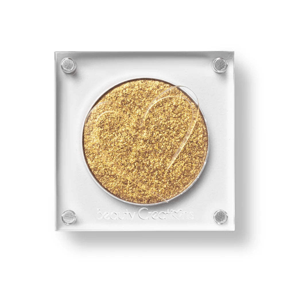 Un estuche cuadrado de sombra de ojos de Beauty Creations en acrílico transparente con un hueco redondo de sombra dorado claro brillante, con un recorte en forma de corazón en la tapa.