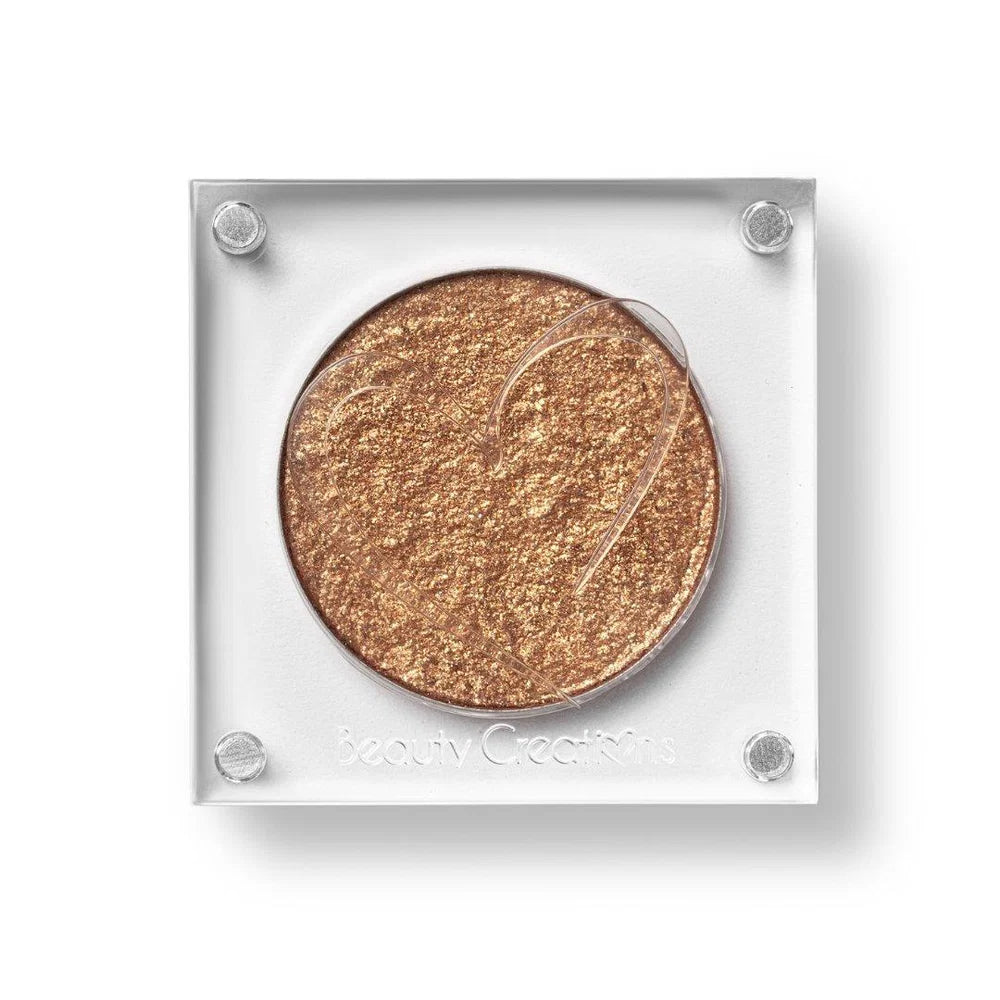 Un estuche cuadrado de sombra de ojos de Beauty Creations en acrílico transparente con un hueco redondo de sombra bronce brillante, con un recorte en forma de corazón en la tapa.