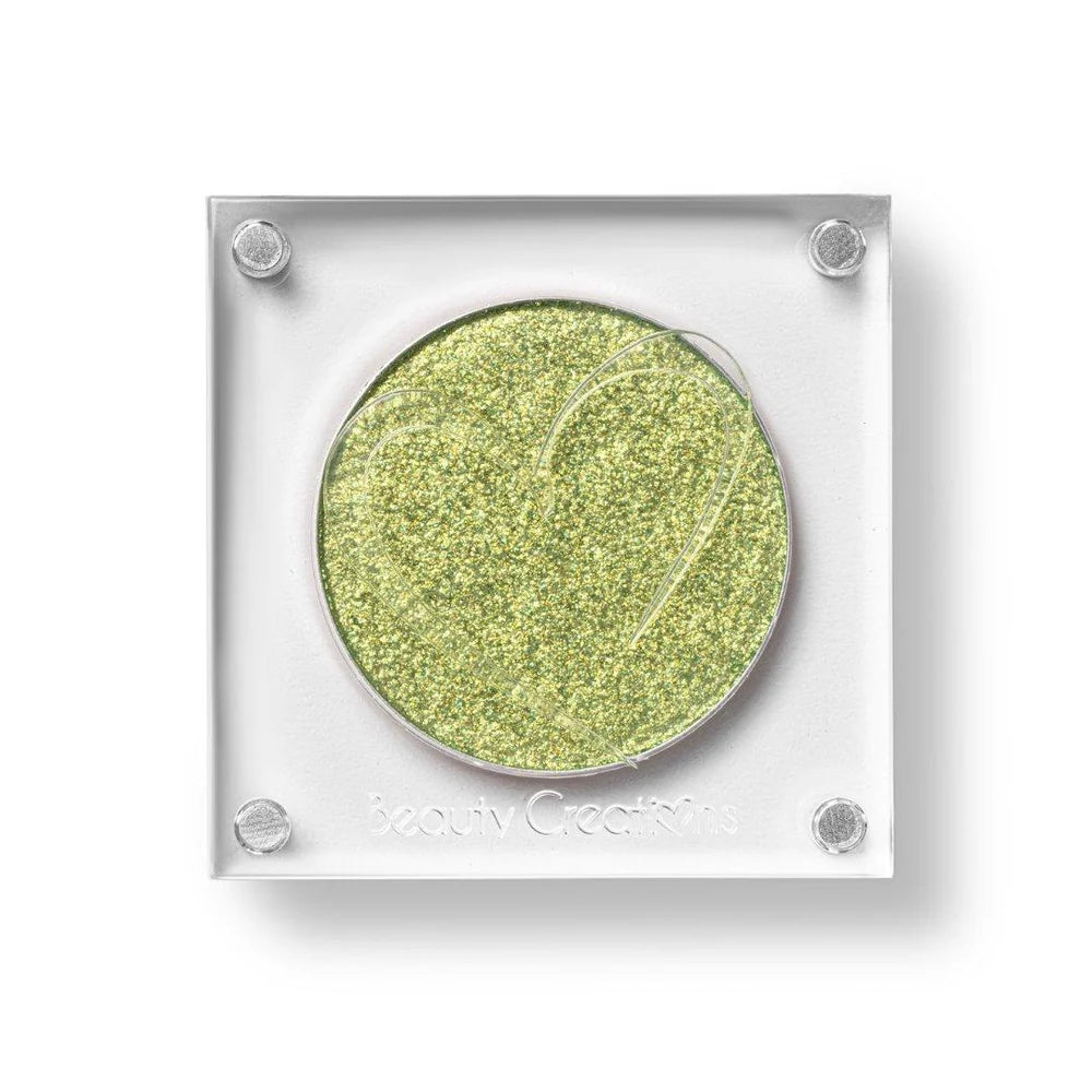 Un estuche cuadrado de sombra de ojos de Beauty Creations en acrílico transparente con un hueco redondo de sombra dorada brillante, con un recorte en forma de corazón en la tapa.