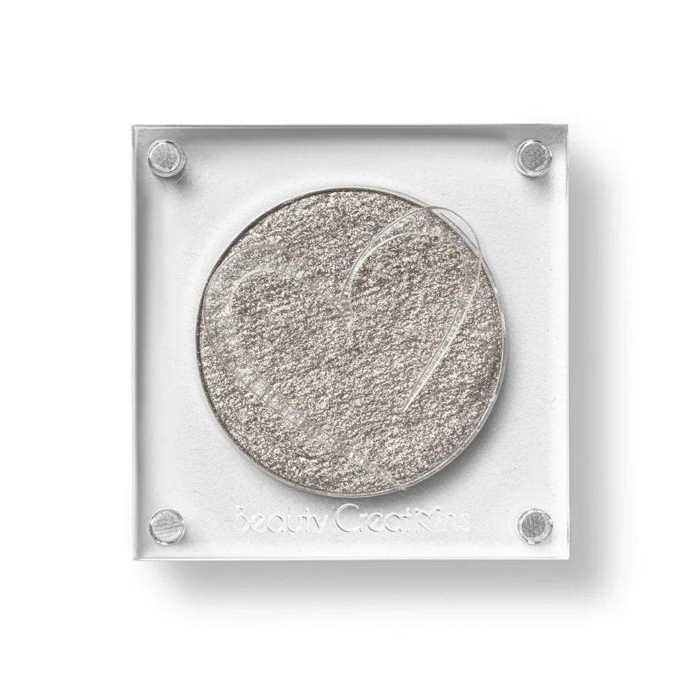 Un estuche cuadrado de sombra de ojos de Beauty Creations en acrílico transparente con un hueco redondo de sombra plateada brillante, con un recorte en forma de corazón en la tapa.