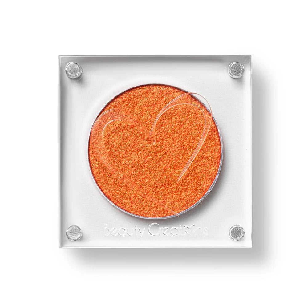 Un estuche cuadrado de sombra de ojos de Beauty Creations en acrílico transparente con un hueco redondo de sombra anaranjado intenso brillante, con un recorte en forma de corazón en la tapa.