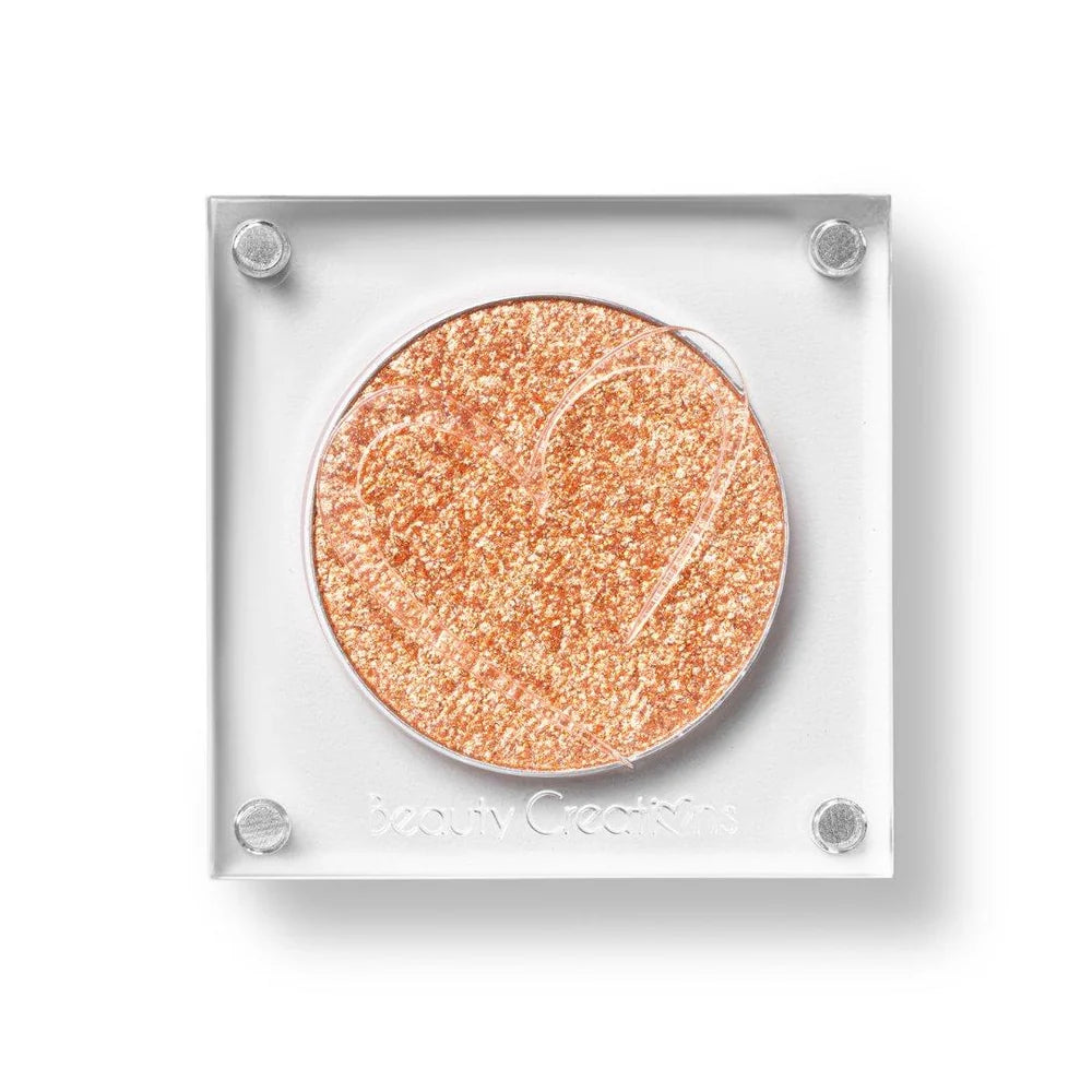 Un estuche cuadrado de sombra de ojos de Beauty Creations en acrílico transparente con un hueco redondo de sombra anaranjado claro brillante, con un recorte en forma de corazón en la tapa.