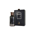 Botella de perfume cilíndrica de vidrio ahumado transparente "Bharara King" de 100 ml con etiqueta vertical negra y tapón metálico en tono bronce/cobre, junto a su lujosa caja negra con patrón geométrico en relieve, marco blanco central y lazo de cinta en la parte superior.
