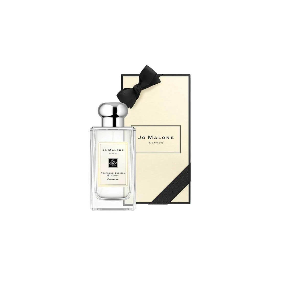 Botella de colonia Nectarine Blossom & Honey de Jo Malone con una tapa plateada pulida, frente a una caja de regalo color crema adornada con un lazo negro, que transmite elegancia y lujo.