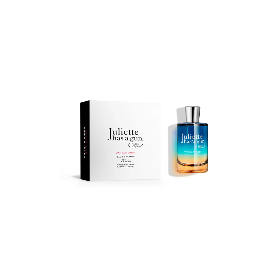 Caja de Vanilla Vibes Eau de Parfum de Juliette Has a Gun junto a una botella de vidrio con un degradado de azul a ámbar, sobre un fondo blanco que transmite una sensación de limpieza y elegancia.