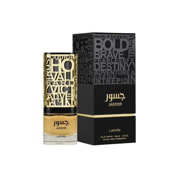 Botella de perfume cilíndrica "Jasoor" de Lattafa de 100 ml con base de vidrio transparente que deja ver el líquido ámbar, coronada por una intrincada funda superior metálica calada en dorado y negro con palabras inspiradoras talladas ("BOLD", "BRAVE", "COURAGEOUS"), junto a su caja negra mate de dos piezas con la mitad superior impresa con tipografía tipográfica en relieve gris y la marca en dorado.