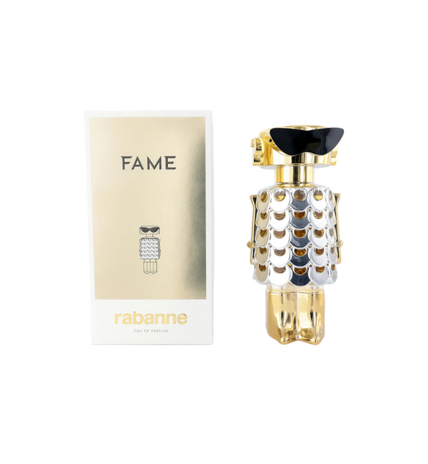 Frasco de perfume y caja de empaque de Rabanne Fame Eau de Parfum sobre fondo blanco. A la izquierda, una caja blanca con un panel central dorado brillante que muestra el nombre "FAME" en la parte superior, una ilustración estilizada de la figura del frasco en el centro y el nombre de la marca "rabanne EAU DE PARFUM" en letras doradas abajo. A la derecha, el frasco en forma de figura futurista metálica con vestido de mallas de lentejuelas plateadas, gafas de sol negras estilizadas y base y detalles en tono 