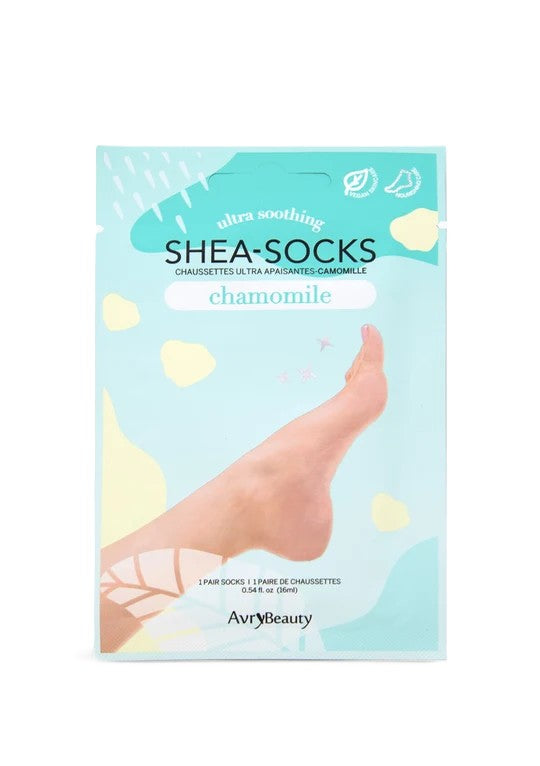 Un empaque turquesa de las mascarillas para pies Shea-Socks de Chamomile muestra un pie descalzo entre suaves formas florales, sugiriendo un cuidado de la piel relajante, tipo spa.