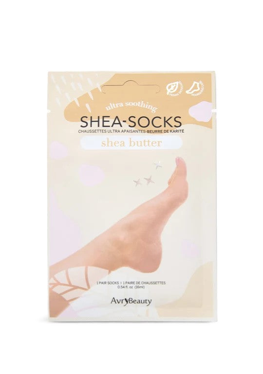 Un empaque crema de las mascarillas para pies Shea-Socks de Shea Butter muestra un pie descalzo entre suaves formas florales, sugiriendo un cuidado de la piel relajante, tipo spa.