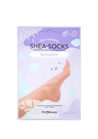 Un empaque violeta de las mascarillas para pies Shea-Socks de Lavender muestra un pie descalzo entre suaves formas florales, sugiriendo un cuidado de la piel relajante, tipo spa.