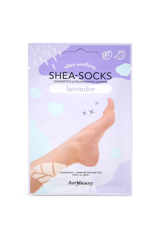 Un empaque violeta de las mascarillas para pies Shea-Socks de Lavender muestra un pie descalzo entre suaves formas florales, sugiriendo un cuidado de la piel relajante, tipo spa.