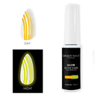 Un frasco de gel para uñas que brilla en la oscuridad de Legacy Nails junto a un tip de uña que muestra rayas amarillo de día y un brillo amarillo intenso de noche.