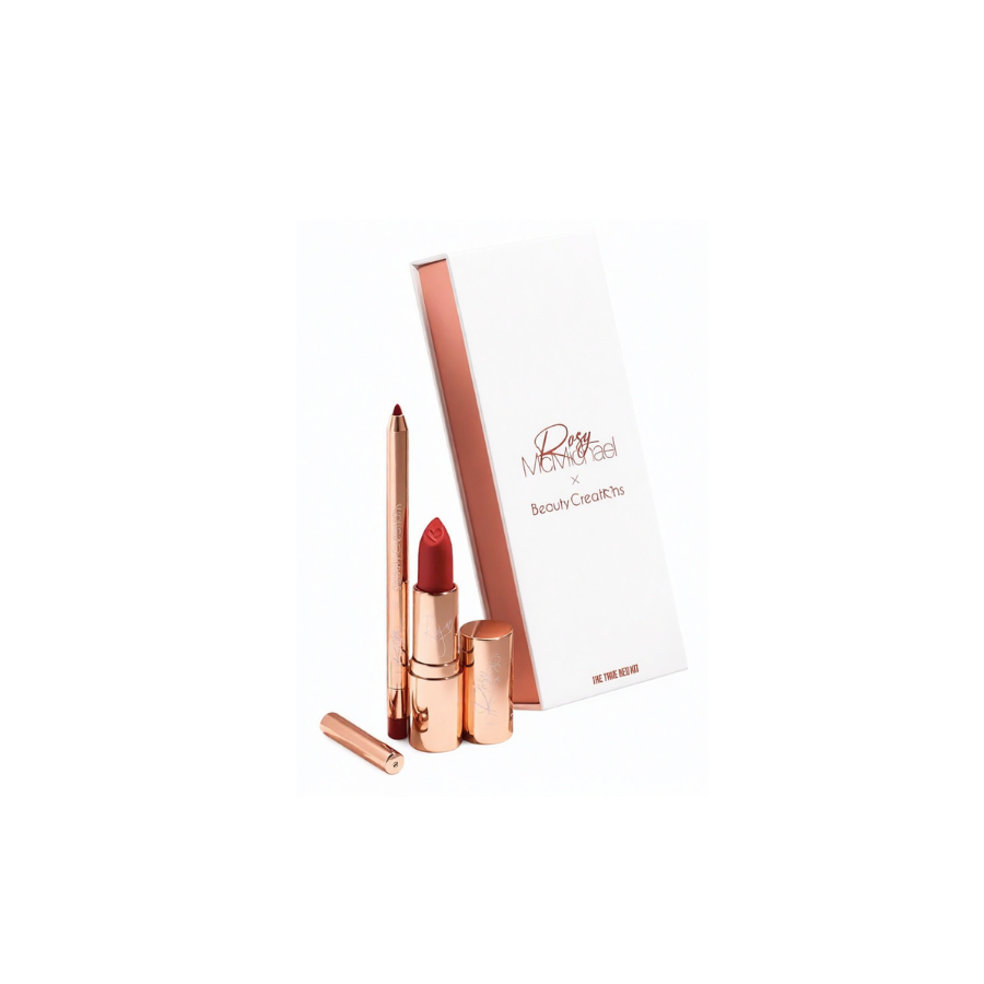 Set de labios rose-gold de Beauty Creations con un labial rojo, lápiz de labios a juego, tubos cosméticos y empaque blanco dispuestos sobre un fondo luminoso.